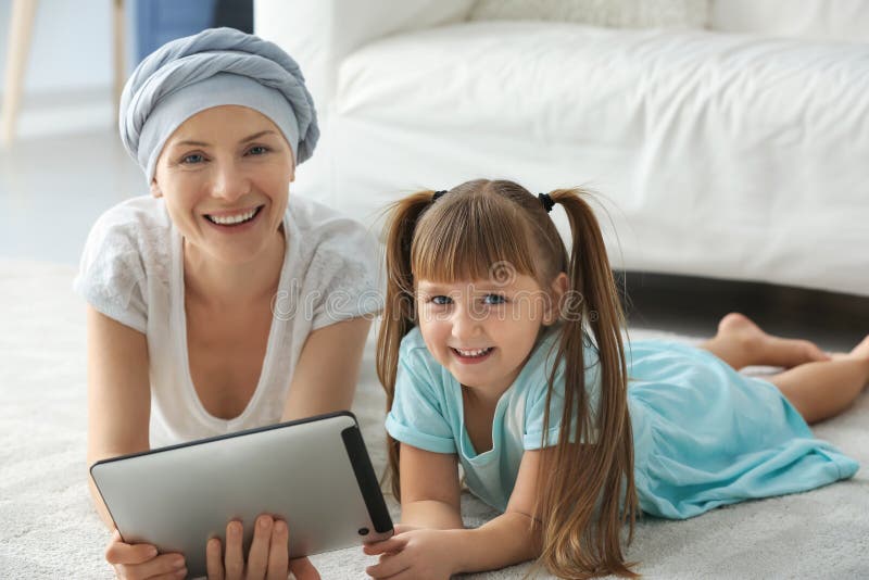 Niña y su madre después de la quimioterapia usando la tableta en casa fotografía de archivo libre de regalías Niña y su madre después de la quimioterapia usando la tableta en casa fotografía de archivo libre de regalías