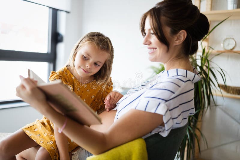 Niña y su madre embarazada leyendo juntos un libro Tiempo de familia imagenes de archivo Niña y su madre embarazada leyendo juntos un libro Tiempo de familia imagenes de archivo