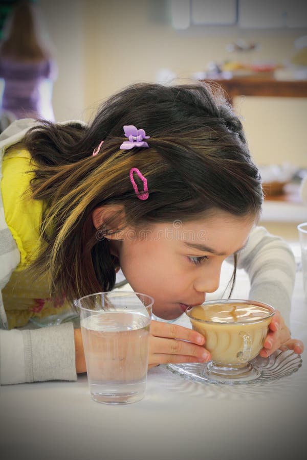 A cute little tween girl leaning forward, carefully sipping tea from a full tea cup in typical little girl fashion. Shallow depth of field. A cute little tween girl leaning forward, carefully sipping tea from a full tea cup in typical little girl fashion. Shallow depth of field.