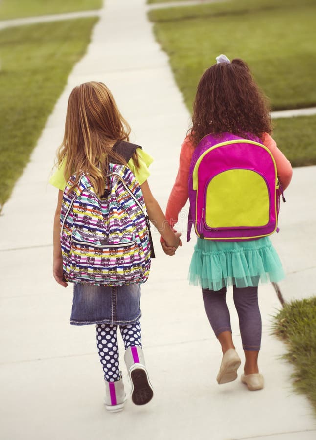 Vintage Tone: Rear view of two little girls holding hands as they walk to school together along the sidewalk. Vintage Tone: Rear view of two little girls holding hands as they walk to school together along the sidewalk