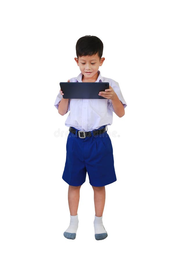 Niño asiático con uniforme en la escuela primaria o primaria jugando a tablet computadora mientras está aislado en fondo blanco. I foto de archivo libre de regalías