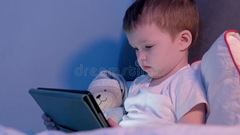 Niño cara iluminada desde la pantalla del portátil mientras juega o aprende a través de internet global. retrato de lindo rubio ca almacen de metraje de vídeo