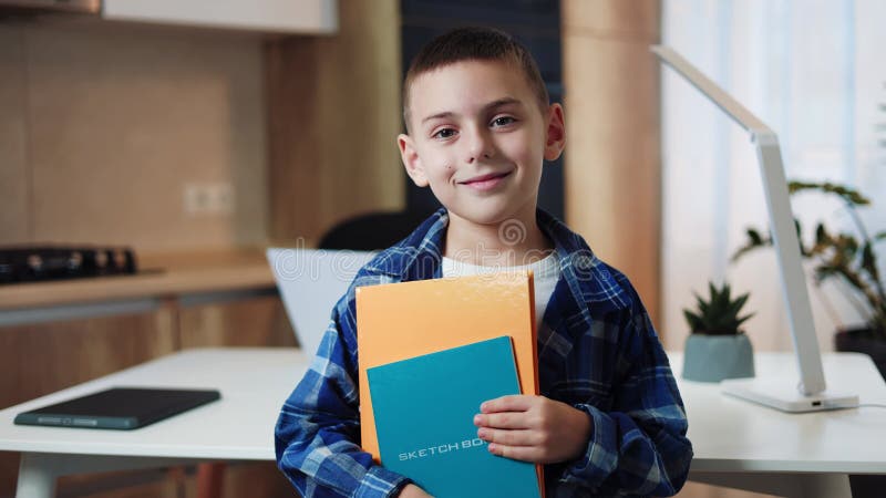 Niño caucásico sonriente vestido con camisa a cuadros que sostiene libros de copias en el interior