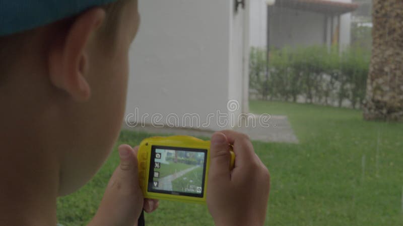 Niño con la cámara que hace las fotos durante día lluvioso