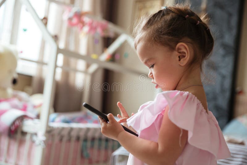 Niño concentrado de la niña dentro usando el teléfono móvil imágenes de archivo libres de regalías Niño concentrado de la niña dentro usando el teléfono móvil imágenes de archivo libres de regalías