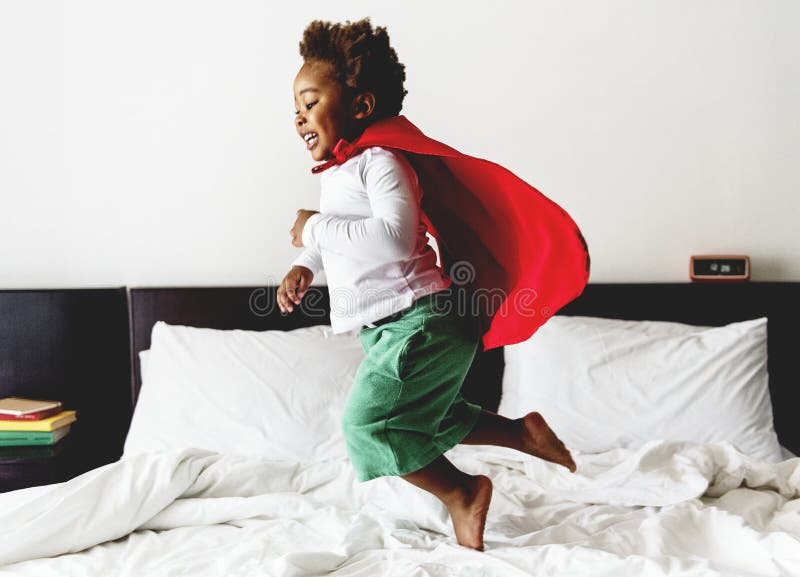 Niño de la ascendencia africana que salta en la cama con el traje