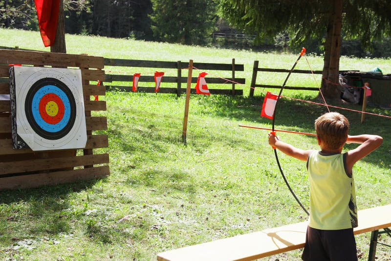 Niño del pelo rubio que juega a tiro al arco durante juegos del verano de los niños