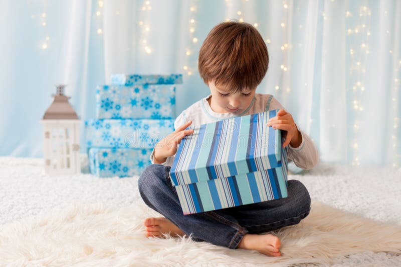 Niño divertido sonriente en el sombrero rojo de Papá Noel que sostiene el regalo de la Navidad en h foto de archivo Niño divertido sonriente en el sombrero rojo de Papá Noel que sostiene el regalo de la Navidad en h foto de archivo