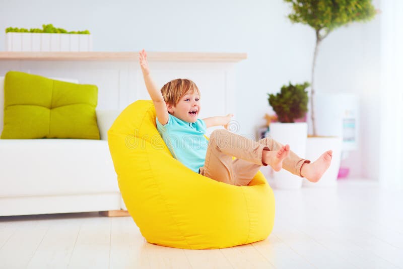 Niño emocionado que se divierte, sentándose en el puf amarillo en casa