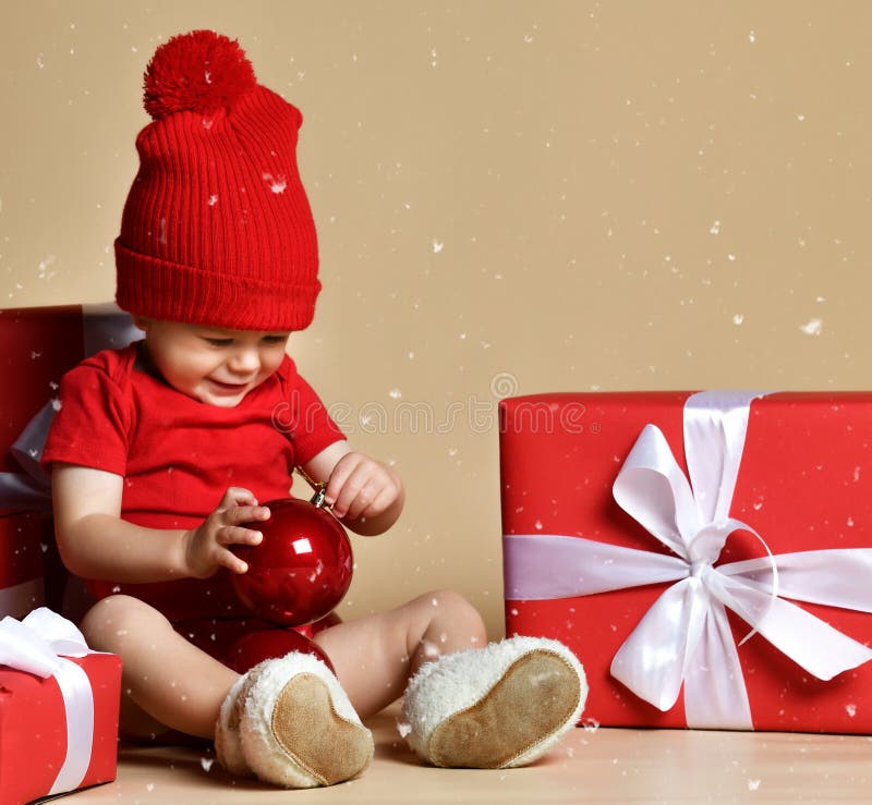 Niño en sombrero rojo con las pilas de actuales cajas alrededor de sentarse en el piso imágenes de archivo libres de regalías Niño en sombrero rojo con las pilas de actuales cajas alrededor de sentarse en el piso imágenes de archivo libres de regalías