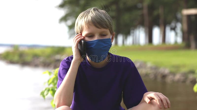 Niño hablando por teléfono celular mientras usa máscara facial durante la pandemia almacen de metraje de vídeo