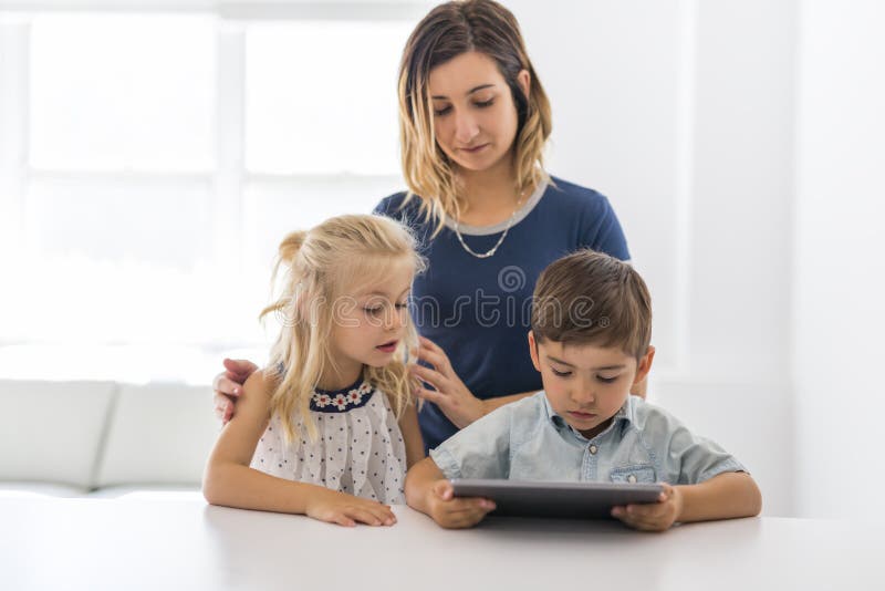 Niño joven adorable del hermano y de la hermana usando la tableta con la madre fotografía de archivo libre de regalías Niño joven adorable del hermano y de la hermana usando la tableta con la madre fotografía de archivo libre de regalías