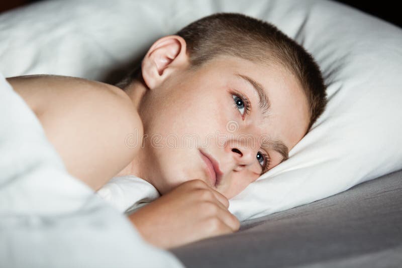 Niño masculino con los ojos abiertos que coloca en la almohada imagen de archivo Niño masculino con los ojos abiertos que coloca en la almohada imagen de archivo
