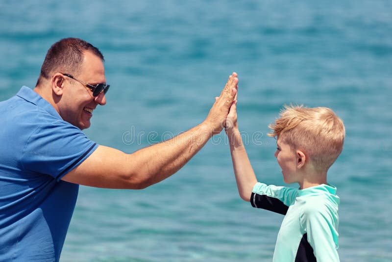 Niño pequeño alegre en el traje de baño que practica surf que da arriba cinco al papá en confianza y confianza de expresión de la