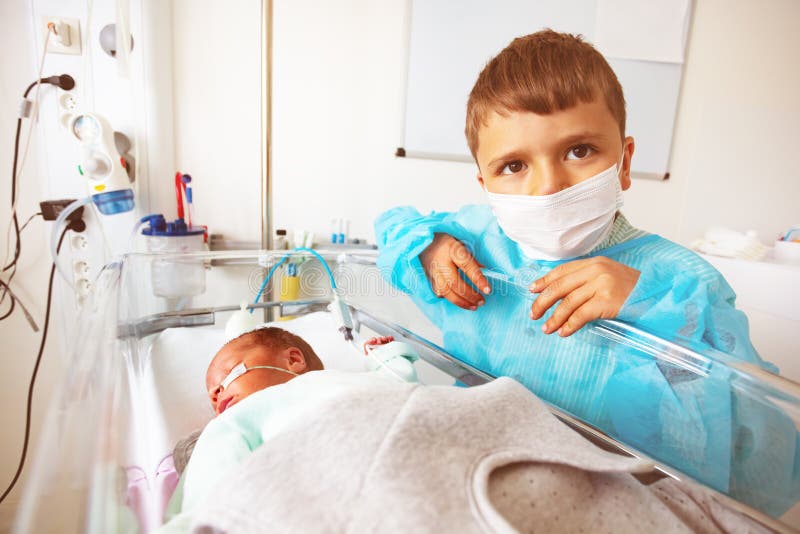 Portrait of the boy and a brother newborn child in the hospital intensive care bed with feeding through nose, constant monitoring. Portrait of the boy and a brother newborn child in the hospital intensive care bed with feeding through nose, constant monitoring