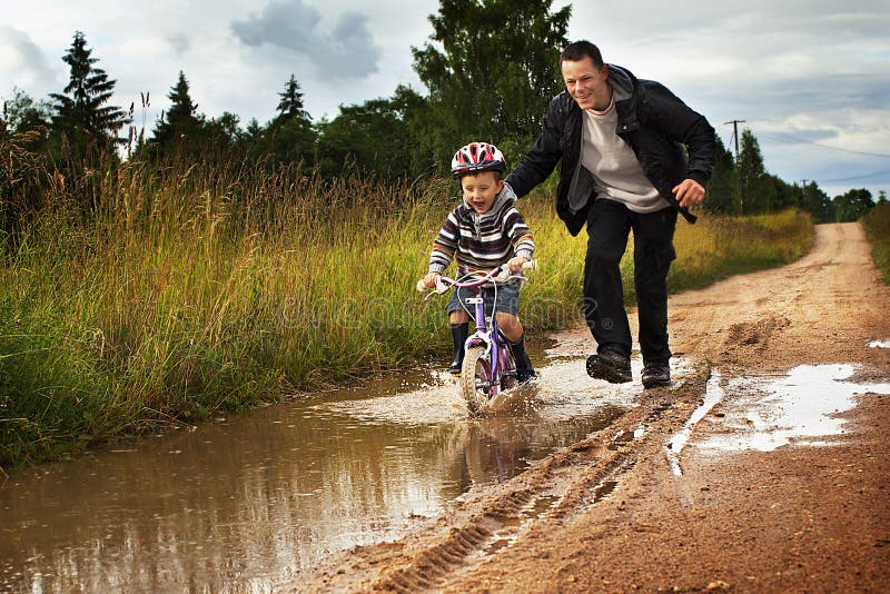Niño pequeño con el papá en una bici después de la lluvia imágenes de archivo libres de regalías Niño pequeño con el papá en una bici después de la lluvia imágenes de archivo libres de regalías