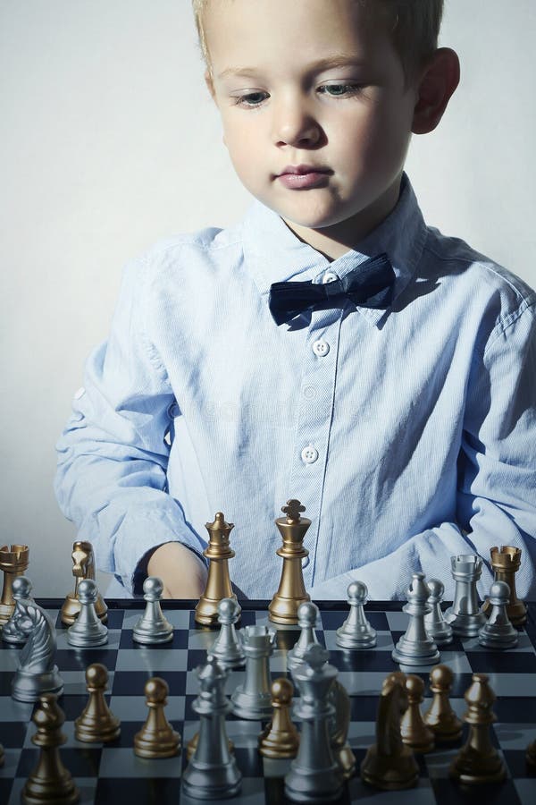 Niño pequeño de moda que juega a ajedrez Pequeño niño del genio Juego inteligente Tablero de ajedrez fotos de archivo libres de regalías Niño pequeño de moda que juega a ajedrez Pequeño niño del genio Juego inteligente Tablero de ajedrez fotos de archivo libres de regalías