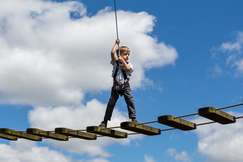 Niño pequeño equilibrado precario en el cable de alta tensión con mirada nerviosa contra el cielo nublado azul en Bristol, Reino fotos de archivo libres de regalías Niño pequeño equilibrado precario en el cable de alta tensión con mirada nerviosa contra el cielo nublado azul en Bristol, Reino fotos de archivo libres de regalías
