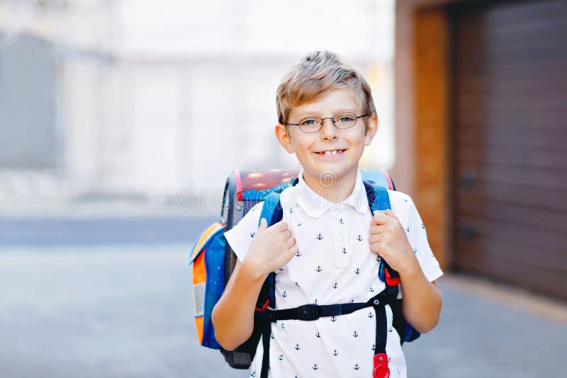 Happy little kid boy with glasses and backpack or satchel. Schoolkid on the way to school. Portrait of healthy adorable child outdoors. Student, pupil, back to school. Elementary school age. Happy little kid boy with glasses and backpack or satchel. Schoolkid on the way to school. Portrait of healthy adorable child outdoors. Student, pupil, back to school. Elementary school age.