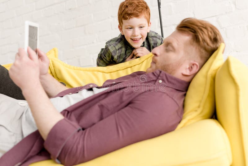 Niño pequeño feliz lindo que mira al padre usando la tableta digital imágenes de archivo libres de regalías