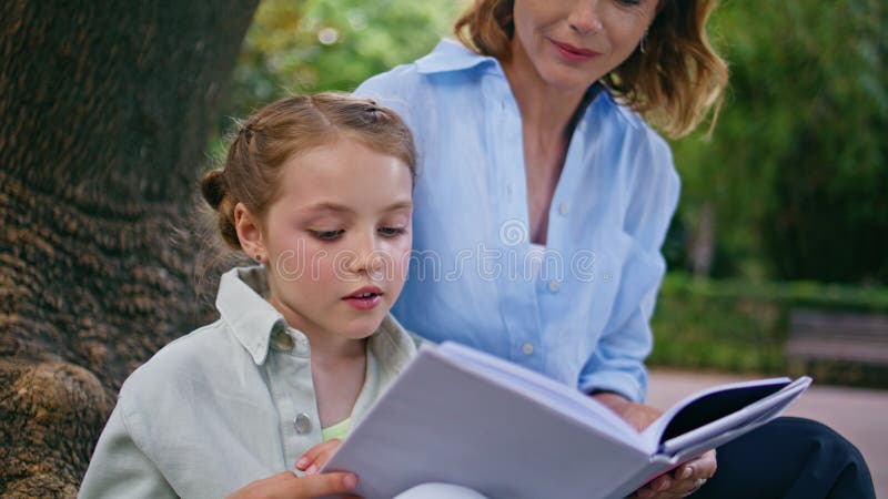 Niño pequeño leyendo cuento de hadas para mamá en el armario del parque. Madre hija disfrutando de un libro foto de archivo libre de regalías