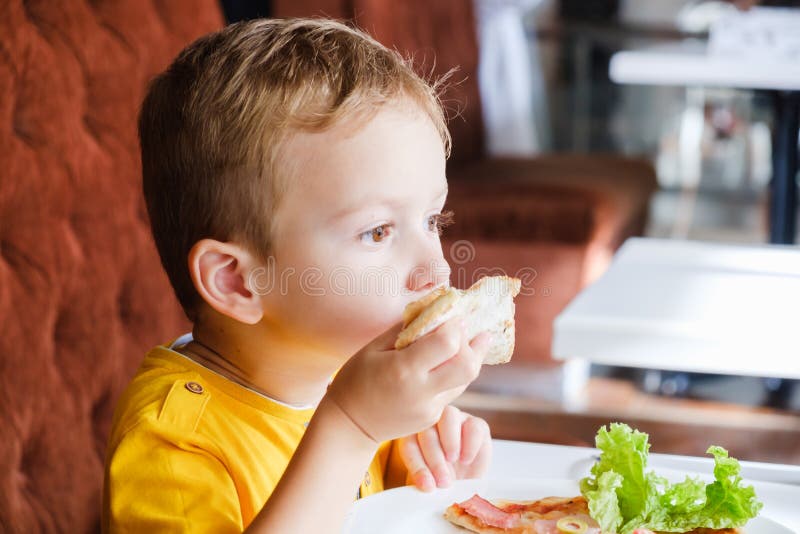 Niño pequeño que come una pequeña pizza fotografía de archivo libre de regalías Niño pequeño que come una pequeña pizza fotografía de archivo libre de regalías