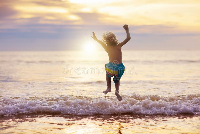 Niño que juega en la playa del océano Niño en el mar de la puesta del sol
