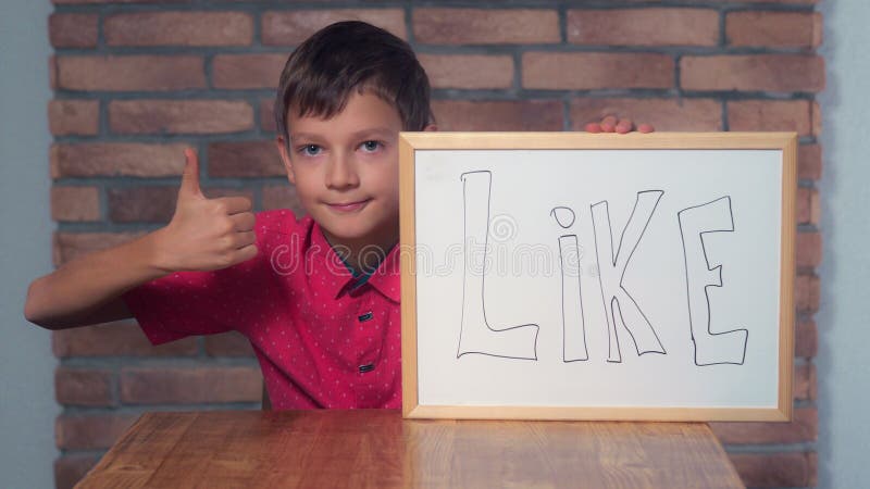 Niño que se sienta en el escritorio que lleva a cabo el flipchart con las letras como fotos de archivo libres de regalías Niño que se sienta en el escritorio que lleva a cabo el flipchart con las letras como fotos de archivo libres de regalías