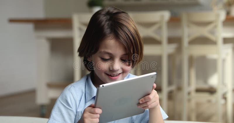 Niño sonriente alegre relajándose solo en casa con dispositivo comprimido