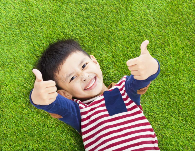 Asian smiling kid lying and thumb up on a meadow. Asian smiling kid lying and thumb up on a meadow