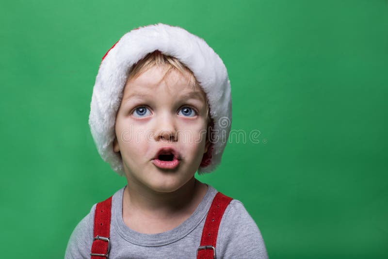 Niño sorprendido con el casquillo rojo de Santa Claus que mira para arriba Ojos azules grandes Concepto de la Navidad fotografía de archivo Niño sorprendido con el casquillo rojo de Santa Claus que mira para arriba Ojos azules grandes Concepto de la Navidad fotografía de archivo