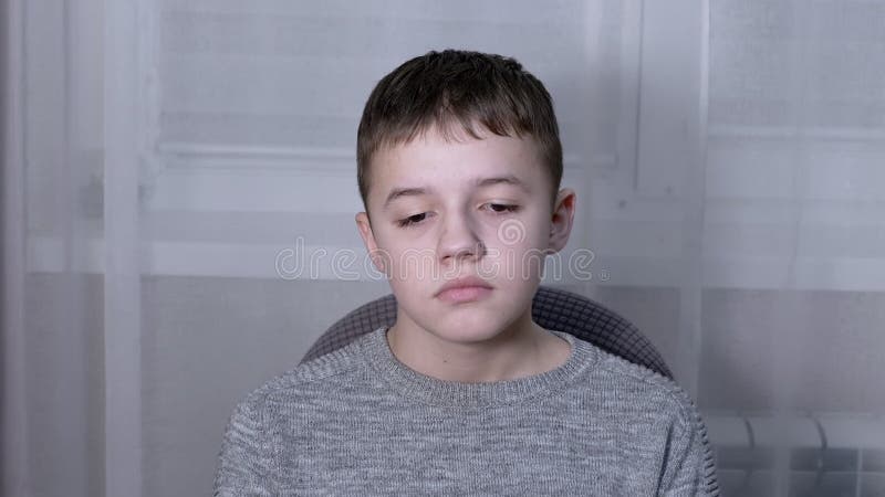 Niño triste y solitario sentado solo en un sillón en una habitación mirando hacia abajo