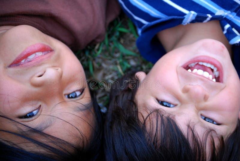 Two children laying in the grass together, close up of their happy faces. Two children laying in the grass together, close up of their happy faces