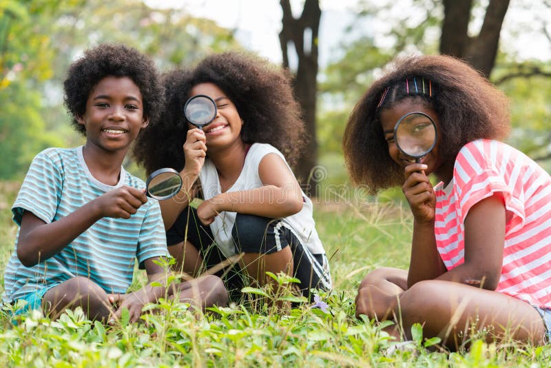 African American children sitting in the grass and looking through the magnifying glass between learn beyond the classroom. .Education outdoor concept. African American children sitting in the grass and looking through the magnifying glass between learn beyond the classroom. .Education outdoor concept