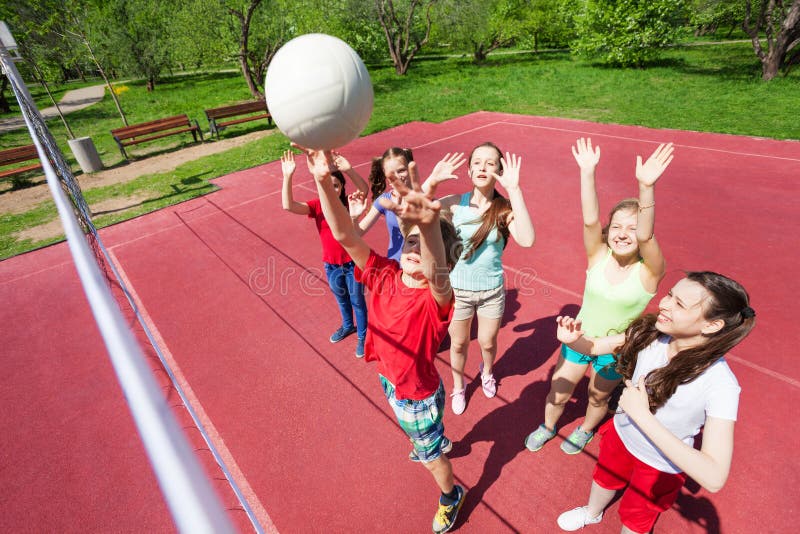 Children with arms up to ball play volleyball near the net on the court during sunny summer day outside. Children with arms up to ball play volleyball near the net on the court during sunny summer day outside
