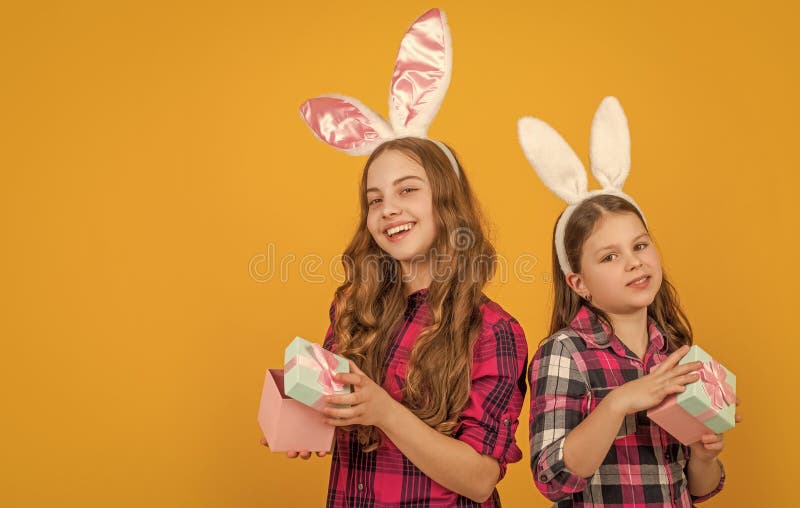 Niños de Pascua sonrientes en los oídos conejidos sostienen la caja de regalo sobre fondo amarillo con espacio para copiar imágenes de archivo libres de regalías