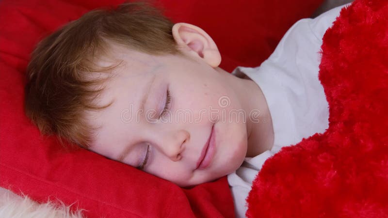 Niños del día de San Valentín. lindo niñito en el día de San Valentín duerme y sonríe sueños mientras abraza un corazón suave y su fotografía de archivo