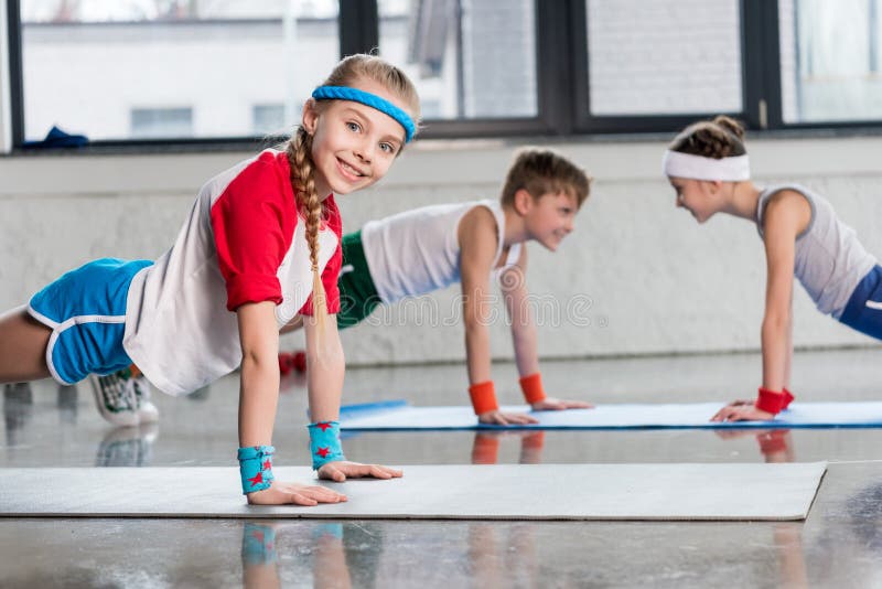 Niños deportivos lindos que ejercitan en las esteras de la yoga en gimnasio y la sonrisa