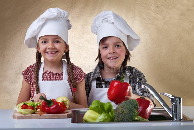 Niños felices que lavan las verduras para una ensalada fotografía de archivo libre de regalías Niños felices que lavan las verduras para una ensalada fotografía de archivo libre de regalías