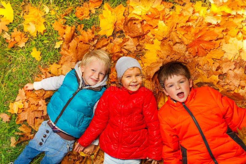 Niños felices que ponen junto en las hojas de otoño fotos de archivo libres de regalías Niños felices que ponen junto en las hojas de otoño fotos de archivo libres de regalías