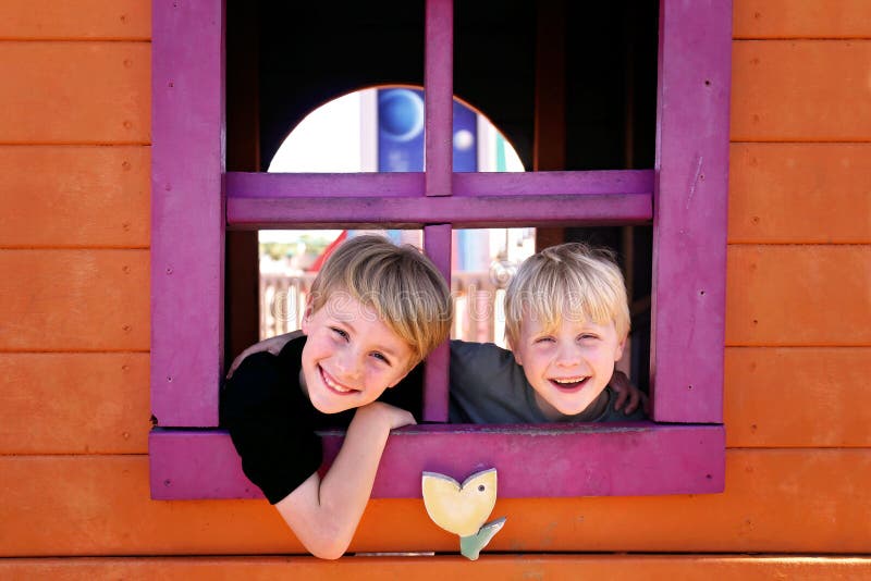 Niños felices que sonríen en el parque como miran a escondidas hacia fuera la ventana de un fuerte del club foto de archivo