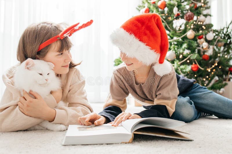 Niños felices, un niño y una niña leen un libro sobre navidad o vísperas de nuevos años en el contexto de una navidad fotografía de archivo