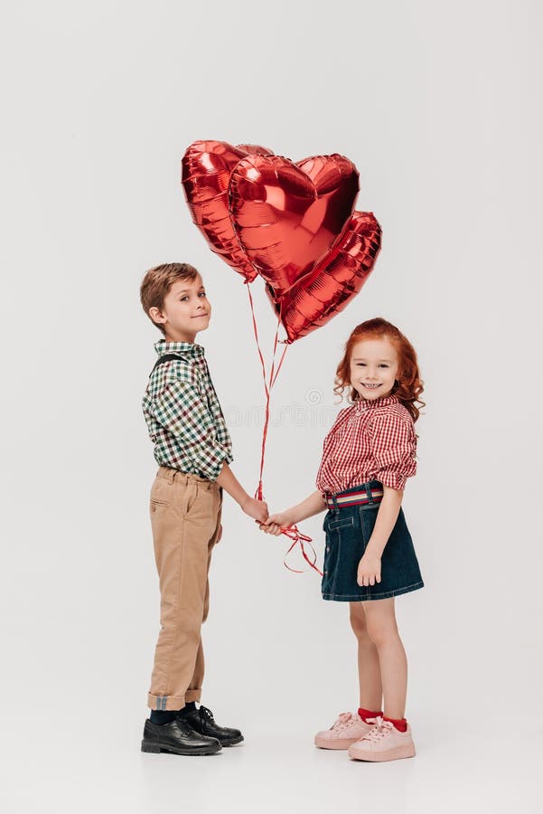 niños lindos que sostienen los globos en forma de corazón y que sonríen en la cámara imágenes de archivo libres de regalías niños lindos que sostienen los globos en forma de corazón y que sonríen en la cámara imágenes de archivo libres de regalías