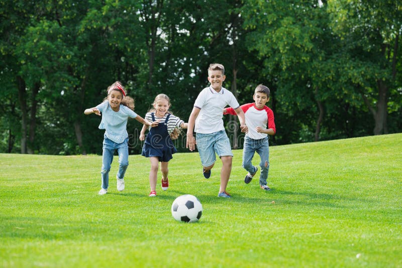 Niños multiétnicos felices que juegan a fútbol con la bola en parque foto de archivo libre de regalías Niños multiétnicos felices que juegan a fútbol con la bola en parque foto de archivo libre de regalías