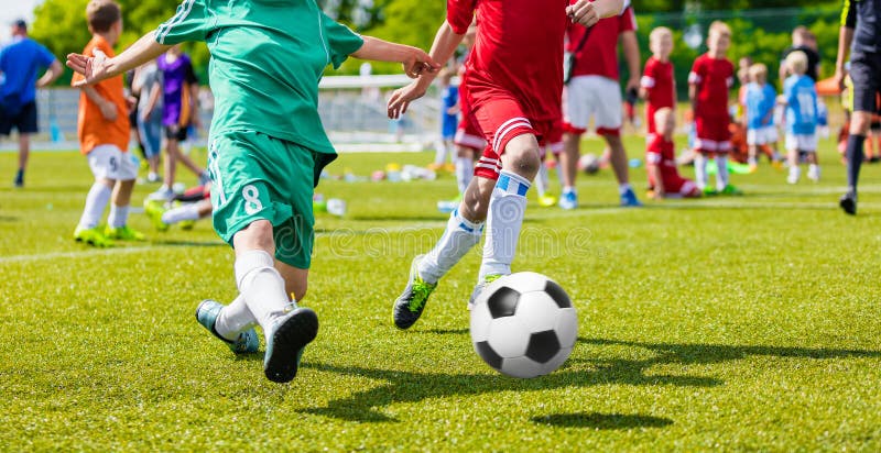 Niños que juegan al juego de fútbol del fútbol en campo de deportes Partido de fútbol del juego de los muchachos en hierba verde