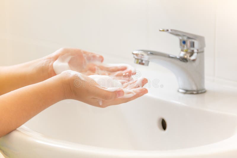 Niños que lavan la mano con el jabón de la espuma en fregadero del cuarto de baño