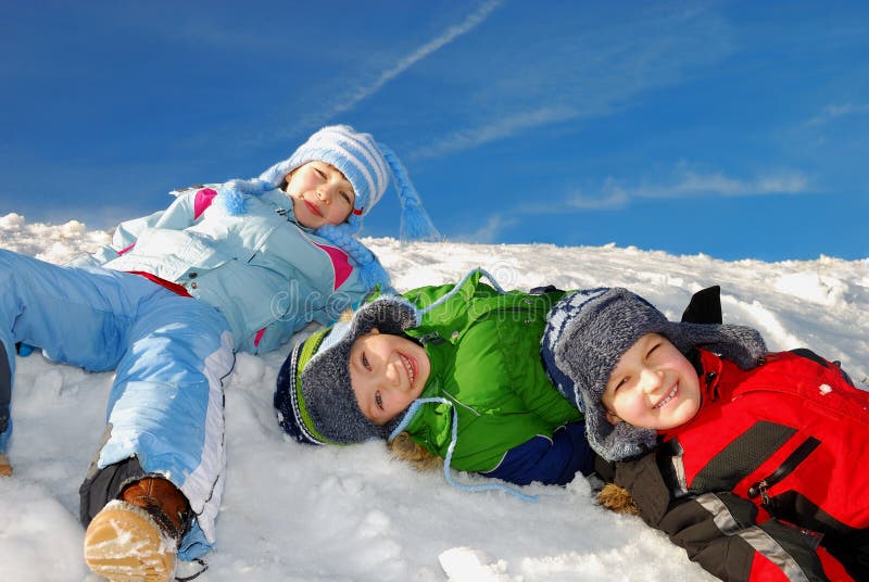 Three happy smiling caucasian white kids in winter clothes lying in the snow and having great fun. Three happy smiling caucasian white kids in winter clothes lying in the snow and having great fun