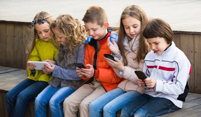 Niños que se sientan con los dispositivos móviles imagen de archivo Niños que se sientan con los dispositivos móviles imagen de archivo