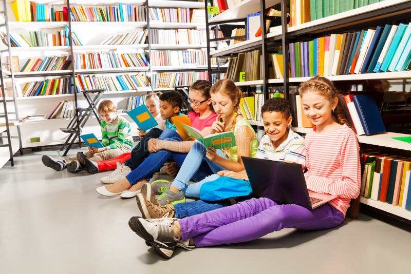 Niños que se sientan en piso en biblioteca y estudiar fotos de archivo Niños que se sientan en piso en biblioteca y estudiar fotos de archivo