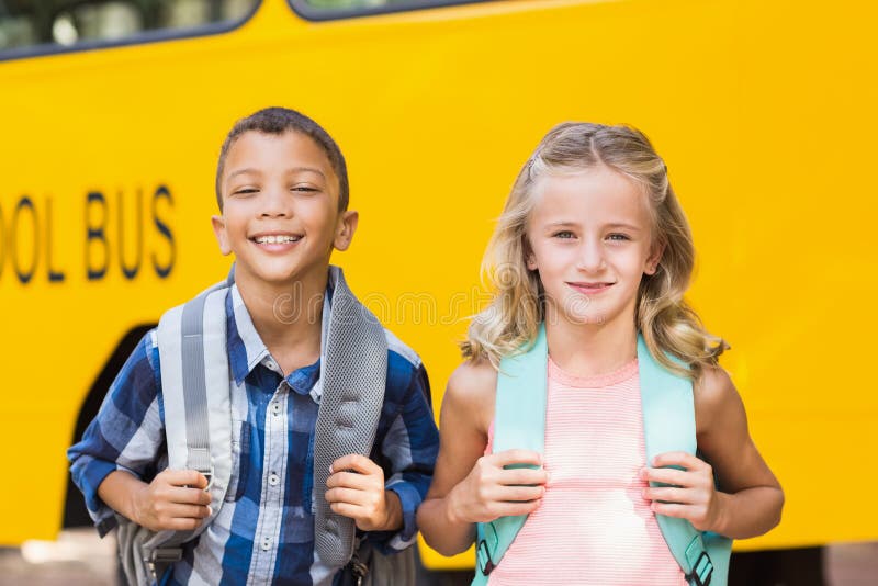 Niños sonrientes que se colocan delante del autobús escolar imagenes de archivo Niños sonrientes que se colocan delante del autobús escolar imagenes de archivo